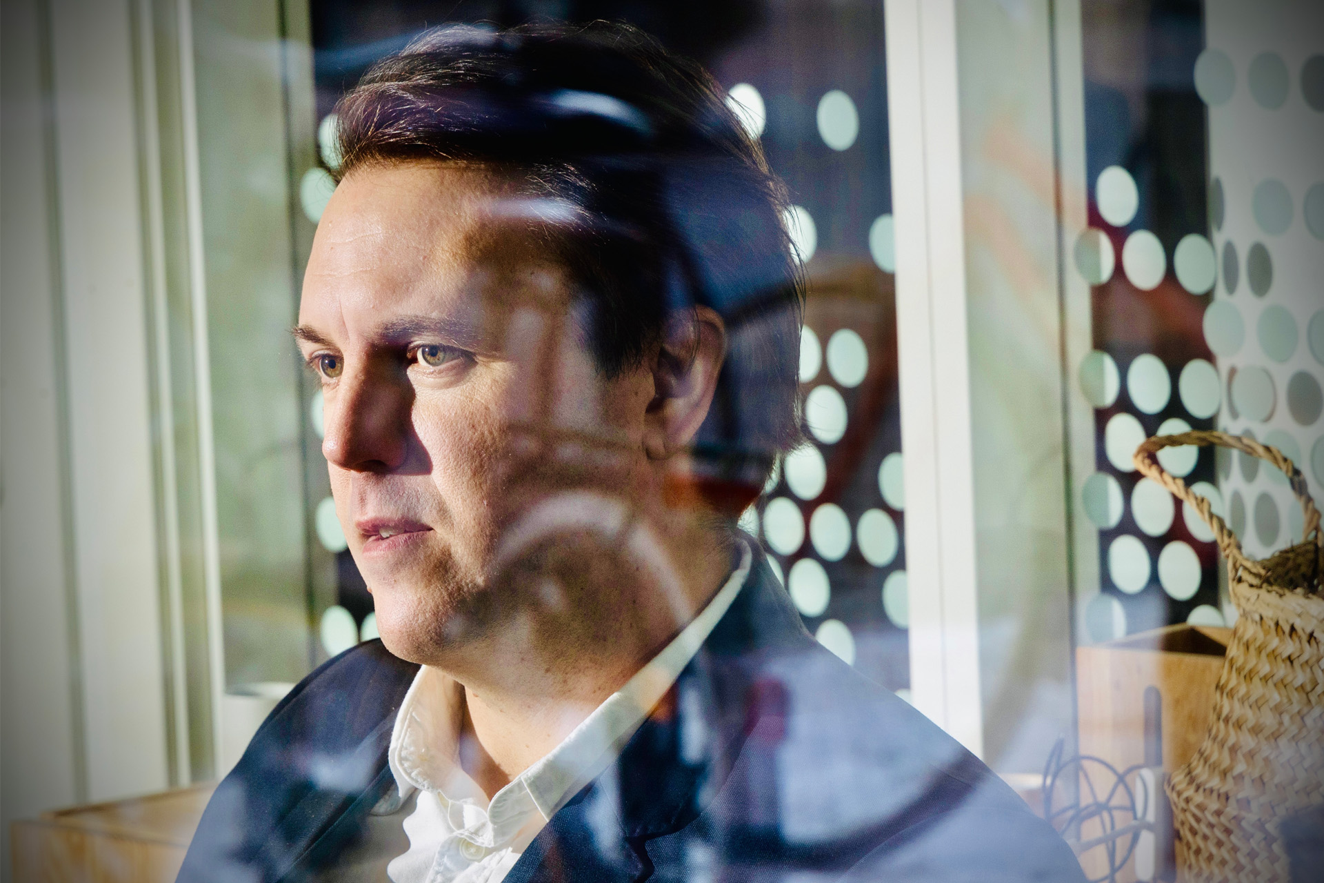 Porträttfoto av en IT-chef taget genom ett fönster med reflektioner. Varmt ljus på ansiktet.